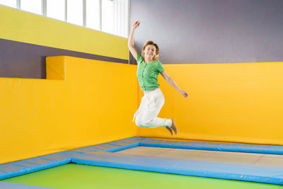 Full length of smiling girl jumping against yellow wall