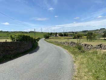 Empty road amidst field against sky