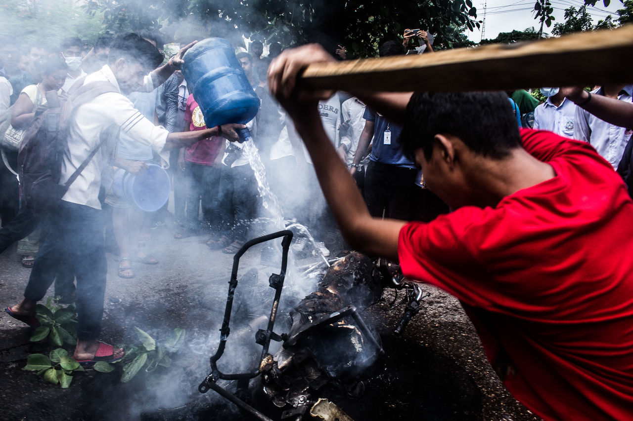 real people, men, smoke - physical structure, water, people, occupation, holding, day, nature, working, motion, casual clothing, outdoors, belief, burning, spraying, preparation