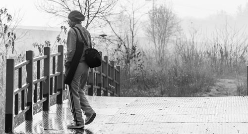 Side view of man standing by railing against bare trees