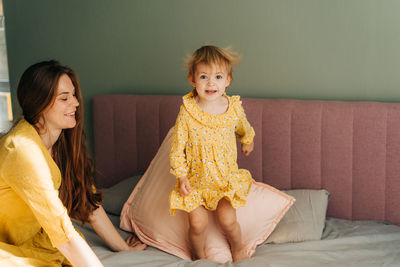 Mommy has fun with little daughter in the bedroom. a little girl in a dress is jumping on the bed.