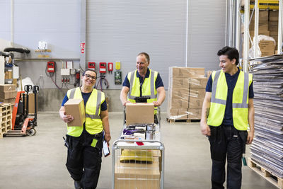 Smiling multi-ethnic coworkers walking with cart at distribution warehouse