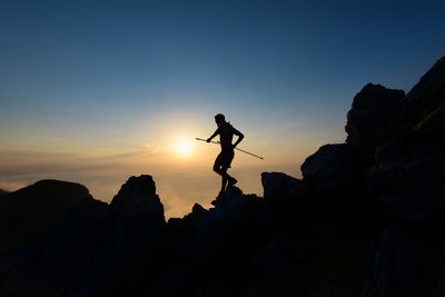 Silhouette man jumping on mountain against sky during sunset