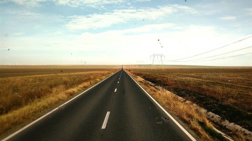 Country road amidst field against sky
