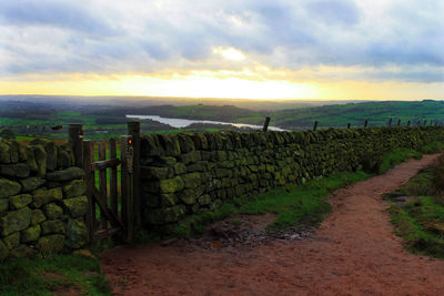 Road by retaining wall against cloudy sky during sunset