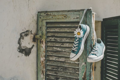 Close-up of shoes with flower hanging on abandoned window