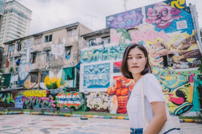 Portrait of teenage girl standing against graffiti wall