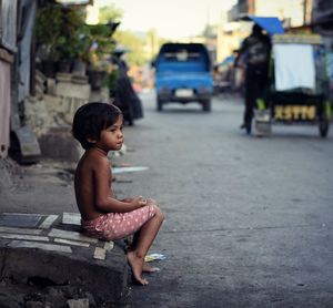 Side view of shirtless boy sitting outdoors