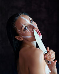 Portrait of young woman wearing mask against black background