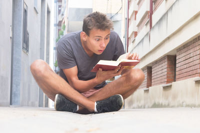 Surprise man reading book on footpath against buildings