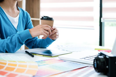 Midsection of businesswoman holding coffee cup while sitting at desk