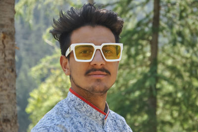 Closeup of a good looking young guy wearing sunglasses, posing outdoor with looking at camera