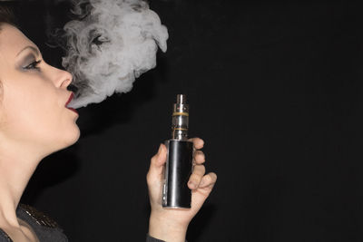 Close-up portrait of woman holding cigarette against black background