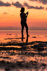 Woman standing at beach against sky during sunset