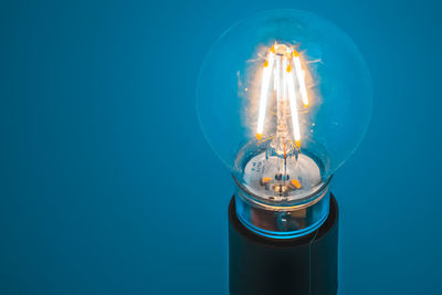 Close-up of illuminated light bulb against blue background