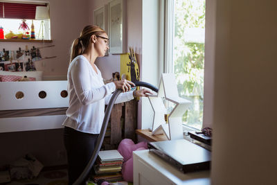 Woman cleaning bedroom with vacuum cleaner at home