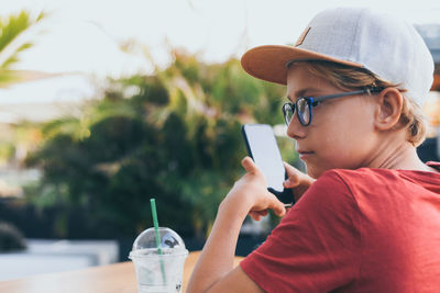 Boy holding smart phone while sitting outdoors