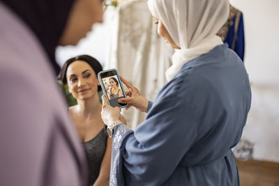 Wedding dress designer photographing bride through smart phone