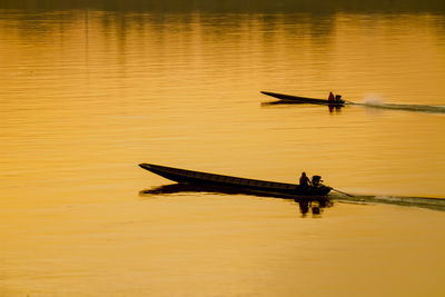 Silhouette man in boat on lake during sunset