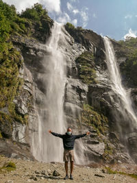 Full length of woman standing on rock at waterfall