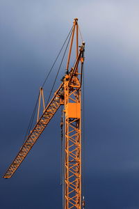 Low angle view of yellow crane against cloudy sky