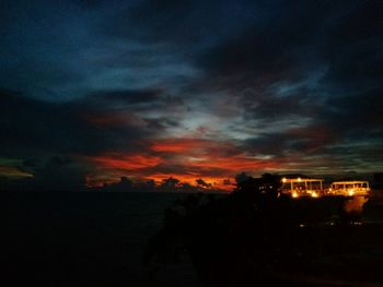 Silhouette houses against dramatic sky at sunset