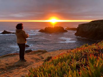 Woman standing on cliff against sea during sunset