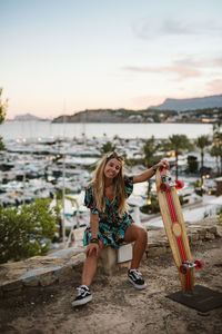 Young female with skate board in front of moraira's yacht club at dusk