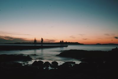 Silhouette people at beach against sky during sunset