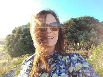 Portrait of smiling young woman against trees on field