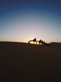 Silhouette man riding motorcycle on desert against clear sky