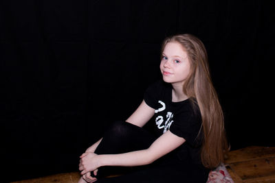 Portrait of young woman sitting against black background