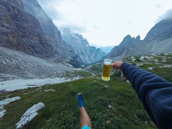 Midsection of person holding drink against mountains
