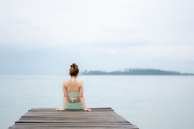 Rear view of woman sitting on pier over sea against sky