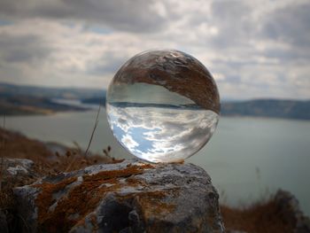 Close-up of crystal ball on rock against sky