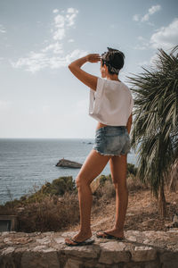 Rear view of woman sitting on retaining wall against sea