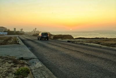 Road by sea against sky during sunset