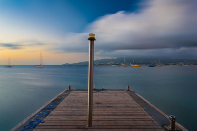 Pole on pier against sea and cloudy sky