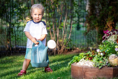 Full length of cute boy holding watering can in yard