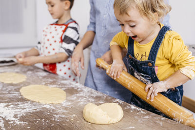 Excited toddler girl rolling out dough with wooden rolling pin