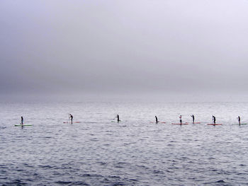 People paddleboarding in sea against sky