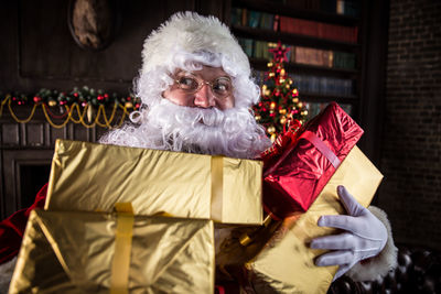 Man wearing santa claus costume holding christmas presents at home