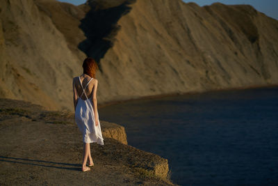 Rear view of woman standing on rock by sea