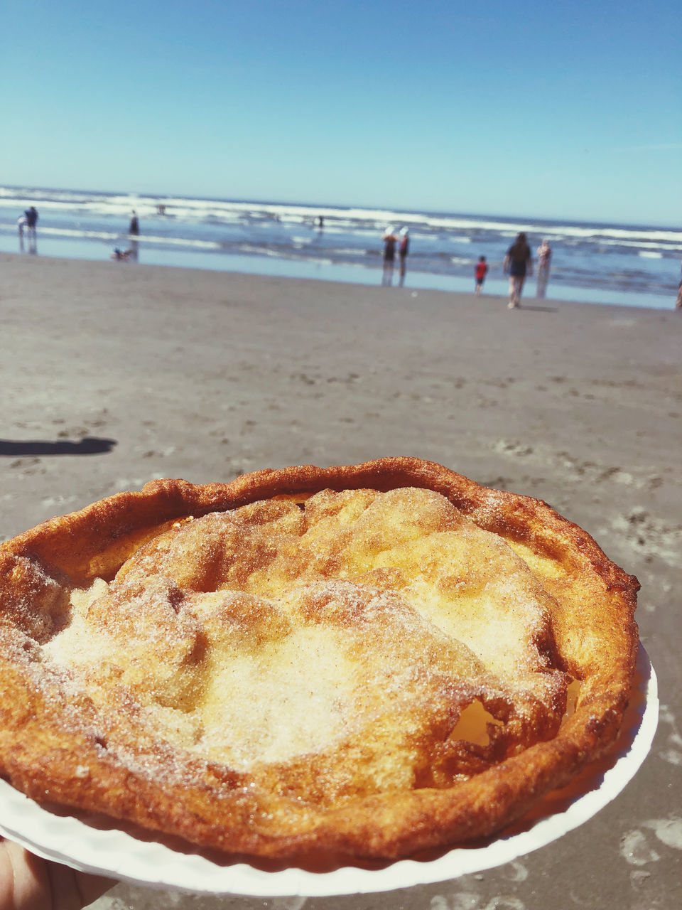 beach, land, sea, food, baked, sand, fast food, food and drink, dish, dessert, water, sky, pie, nature, holiday, day, sweet food, apple pie, horizon over water, hand, horizon, close-up, freshness, focus on foreground, leisure activity, one person, lifestyles, sweet, cuisine