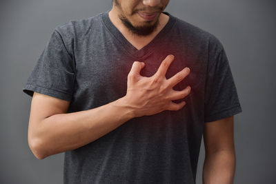 Midsection of man with chest pain against gray background