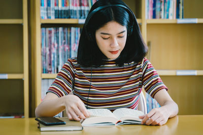 Young woman reading book while listening music on table