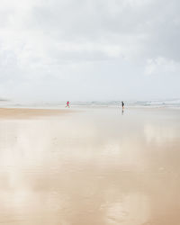 Children playing at beach against cloudy sky