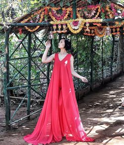 Woman wearing pink dress looking at floral garland while standing on covered walkway