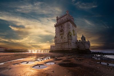 Low angle view of historic building by sea against sky at sunset