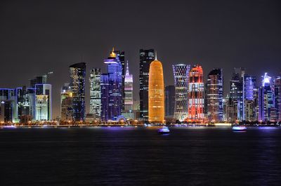 Illuminated buildings by river against sky at night